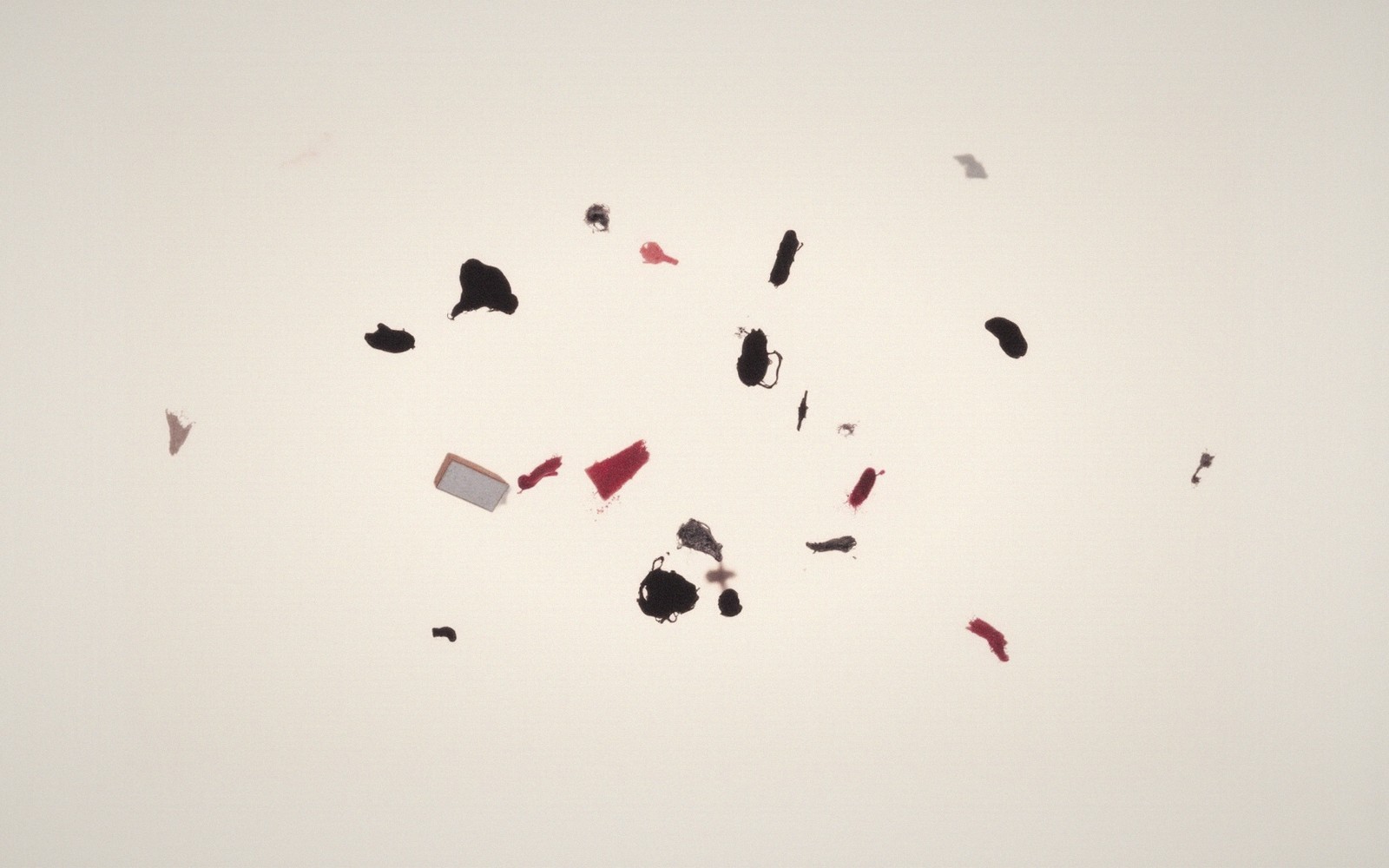Scattered black and red fragments and a small mirror shard on a pale background